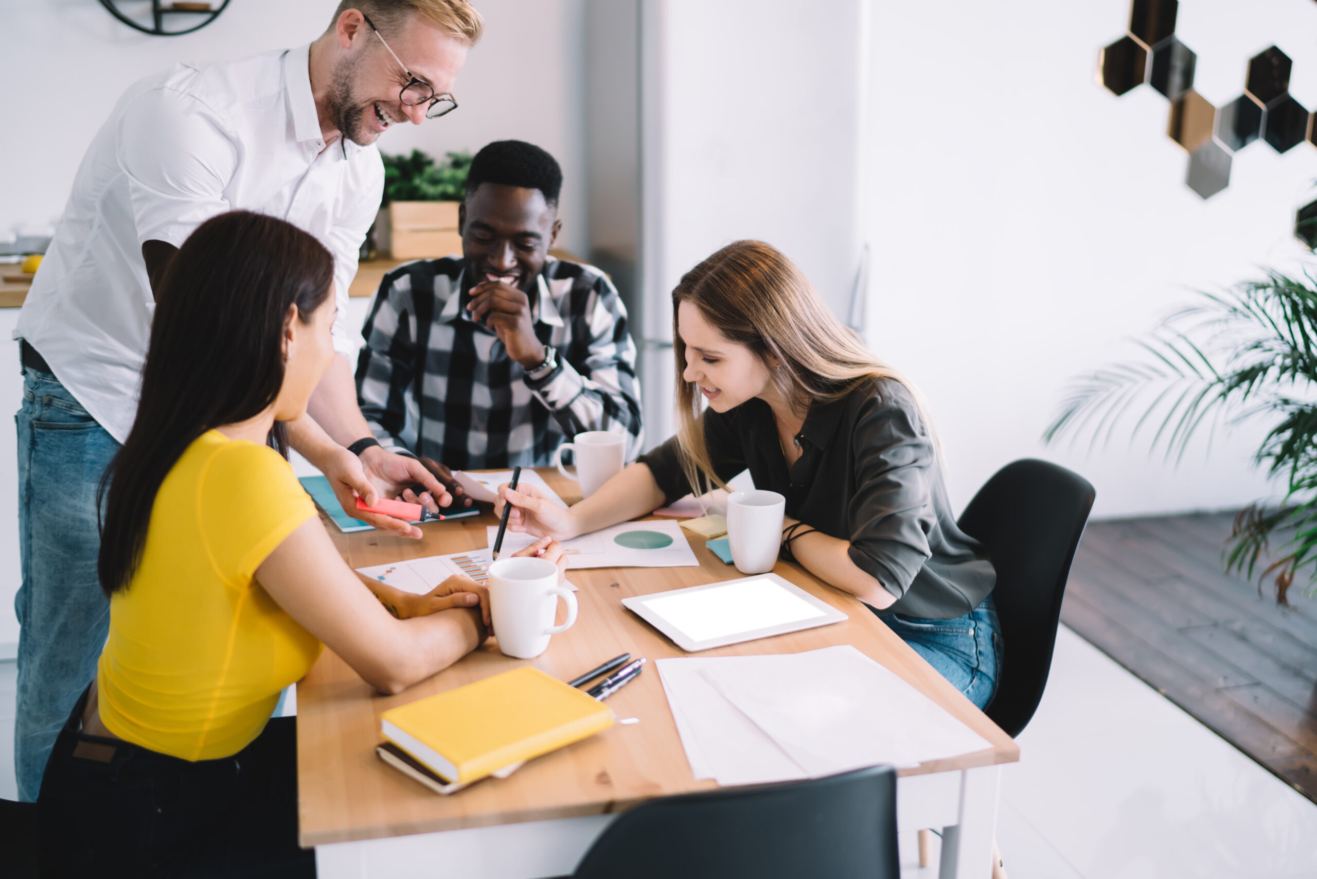 Optimistic diverse colleagues writing plan High angle of optimistic multiracial coworkers in casual wear smiling and working with documents while having meeting at wooden table